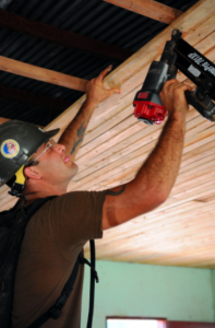 A man using a nail gun to attach wood to a ceiling 